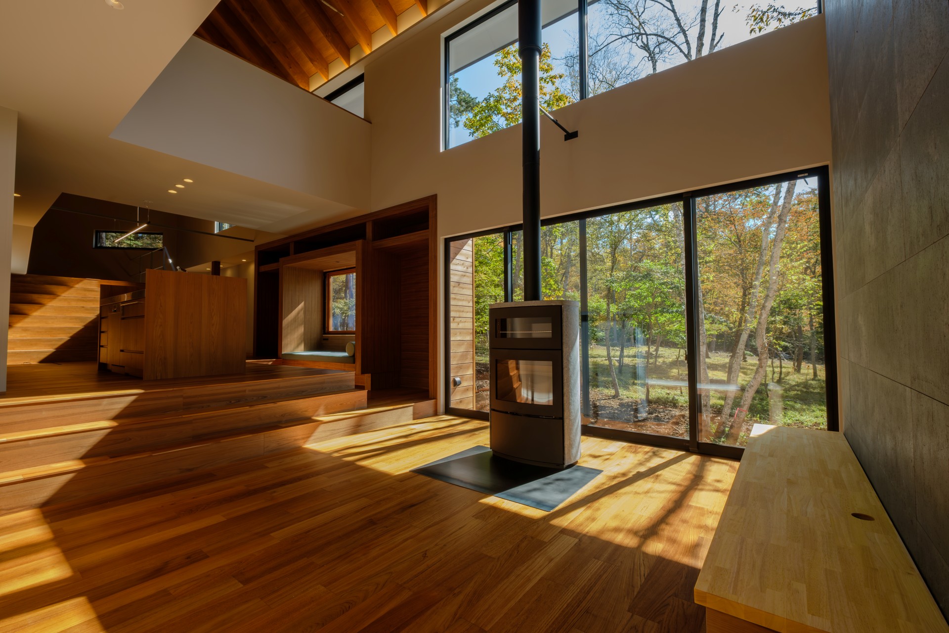 蓼科八ヶ岳地域に建つ、内装をチーク材と木材で仕上げた高級別荘。薪ストーブがあるリビング吹き抜け空間から望む白樺の景色