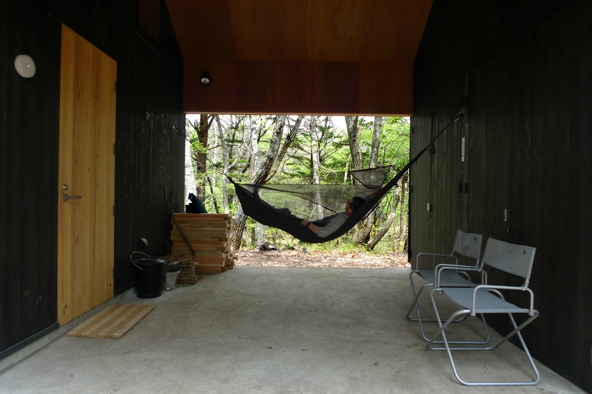 蓼科八ヶ岳地域に建つ、大自然の中で遊ぶ為の杉板無垢材の外壁で出来たミニマルな山小屋（別荘）。屋根付きの屋外土間空間でバーベキューやハンモックで遊ぶ