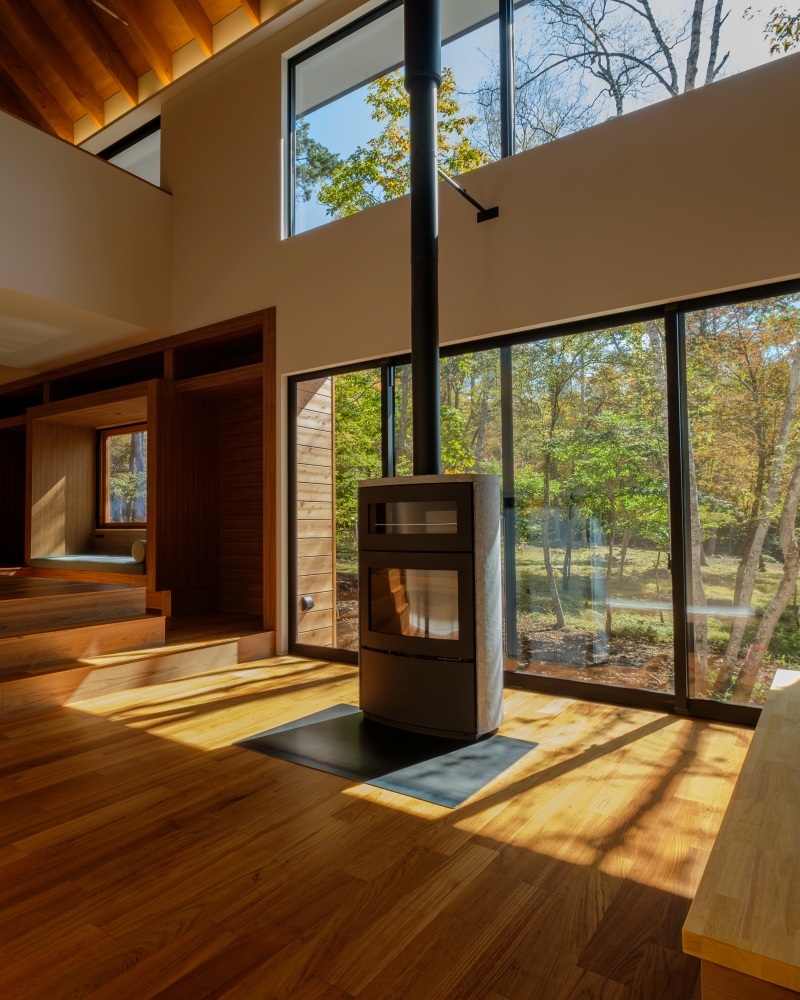 蓼科八ヶ岳地域に建つ、内装をチーク材と木材で仕上げた高級別荘。薪ストーブがあるリビング吹き抜け空間から望む白樺の景色