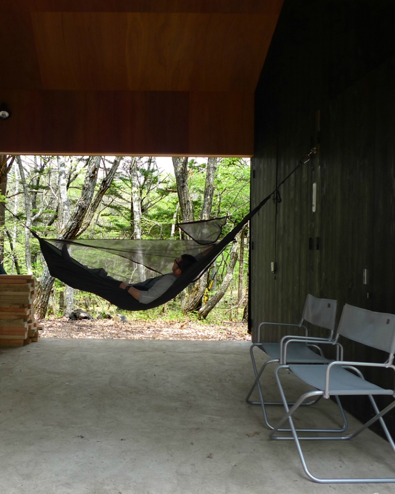 蓼科八ヶ岳地域に建つ、大自然の中で遊ぶ為の杉板無垢材の外壁で出来たミニマルな山小屋（別荘）。屋根付きの屋外土間空間でバーベキューやハンモックで遊ぶ